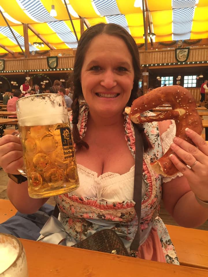 A person holding a large glass of beer and a pretzel

Description automatically generated
